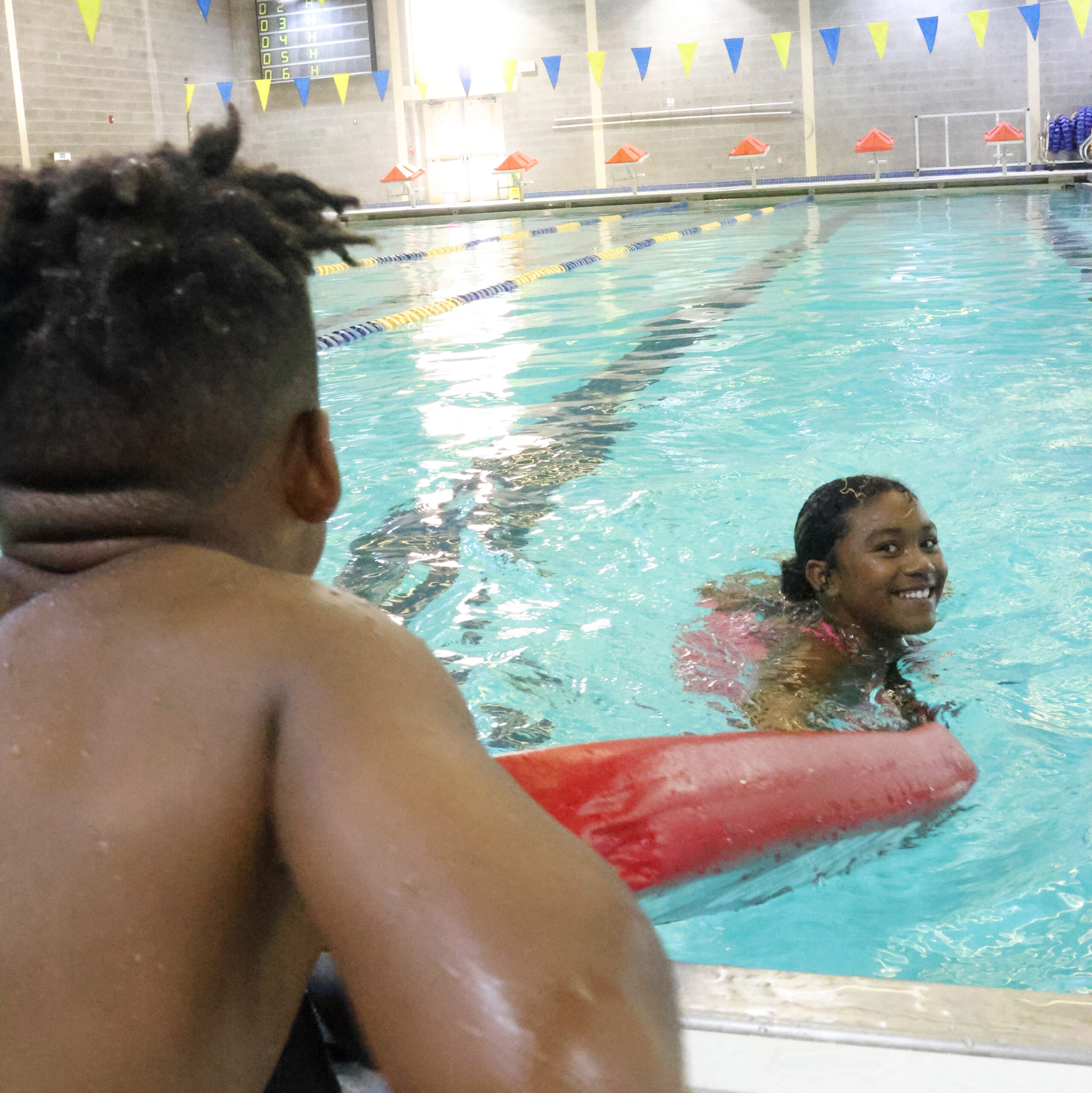 a child holding lifeguard rescue tube to other child in a pool
