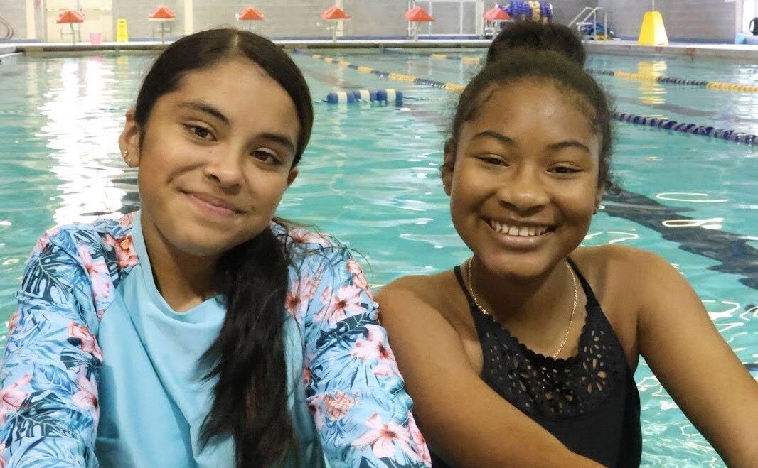 Two young girls smiling while standing in a pool