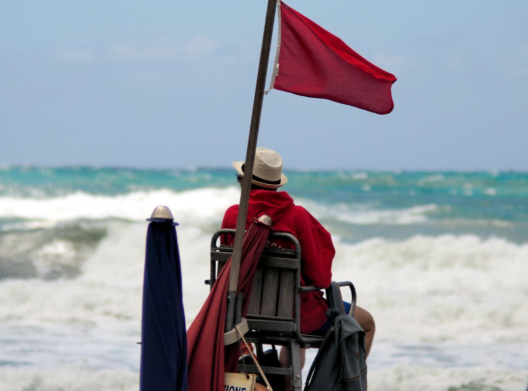 Lifeguard watching over with red flag behind him